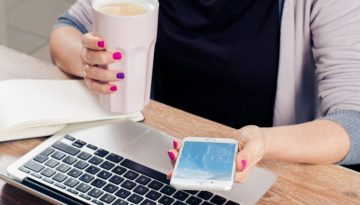woman-holding-coffee-mug-and-text-messaging-with-laptop-on-wooden-table