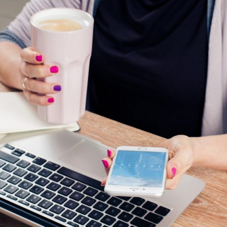 woman-holding-coffee-mug-and-text-messaging-with-laptop-on-wooden-table